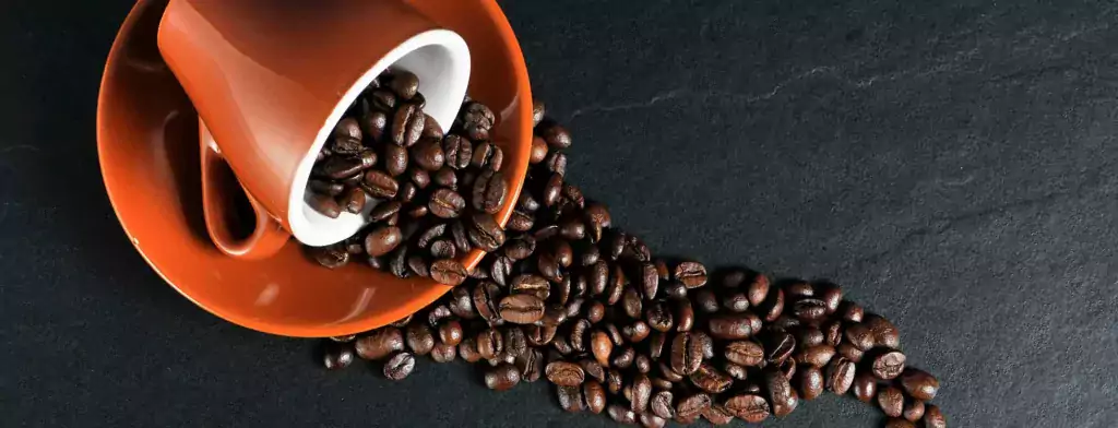 Coffee beans spilling from orange cup